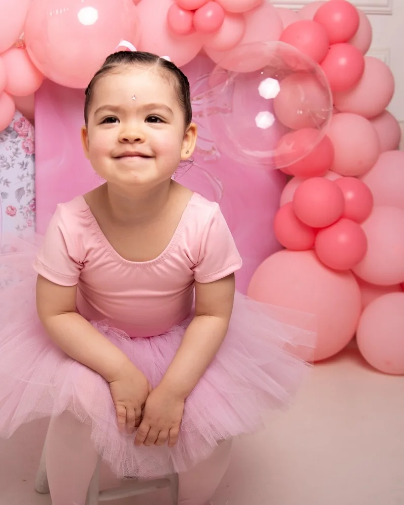 Niña con tutú rosa sonriendo entre globos rosados